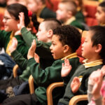 children in green school uniforms doing hand movements