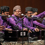 A seated group of men in purple shirts with microphones and instruments