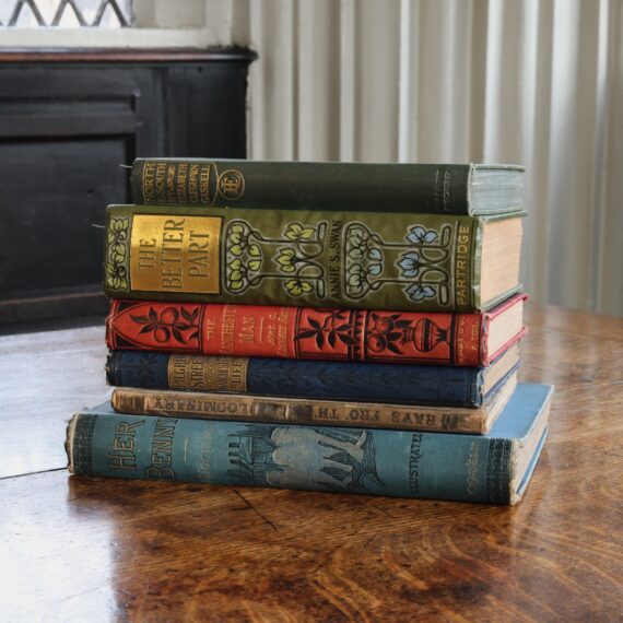 A pile of books with brightly-coloured historic bindings on a wooden desk. The spines of the books are facing forwards.