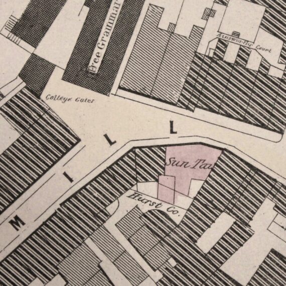 An old map of Manchester that has been coloured in pale pink and blue. It shows the Sun Inn opposite the entrance to Chetham's Library on Long Millgate.