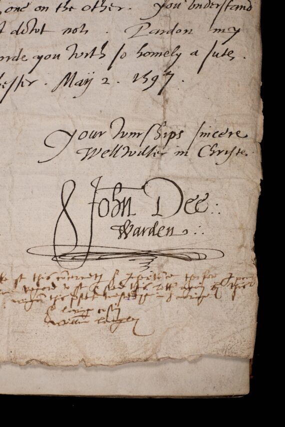 The corner of a sheet of sheet of paper containing a letter. A cursive hand has written ‘Your wurships sincere wellwisher in Christe’, and beneath it written ‘John Dee: Warden’.