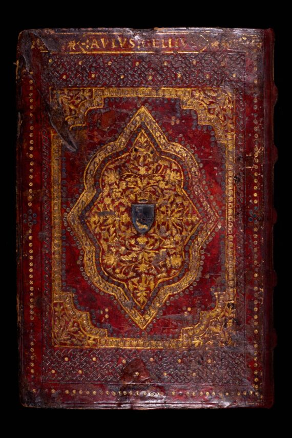 The cover of a book bound in deep red leather, with an elaborate gild-stamped geometric design. At the centre of the design is a shield shape, now black, which contains a raven in relief. At the top of the book, the name of the work’s author, Aulus Gellius, is stamped within a border.