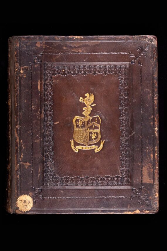 A book bound in dark brown leather, now quite scuffed. In the centre of the cover is a gilt-stamped armorial design featuring the arms of Humphrey Chetham, and beneath it, a scroll bearing the motto ‘QUOD TUUM TENE’. Around the edges is a blind-stamped decorative border, and in the bottom left corner of the cover is a round label bearing the shelfmark ‘7.B.3.7’.