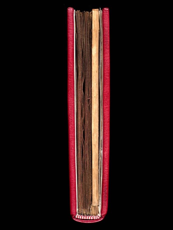 A medieval manuscript bound in red leather, seen from above. A stained white card insert is visible to the right of the textblock. The manuscript has an endband made from alternating red and white thread.