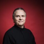 Conductor Mark Elder against red backdrop