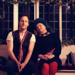 Eliza Carthy and Jon Boden seated against a window with christmas decorations