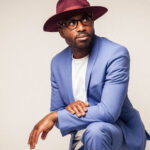 Artist Alexis Ffrench, wearing a pale blue suit and a broad-brimmed hat