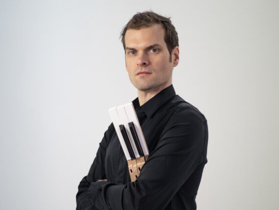 Jazz pianist Andrew McCormack dressed in black holding piano keys against grey background