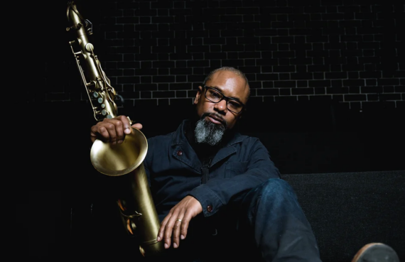 Jazz performer Denys Baptiste with saxophone against a black background