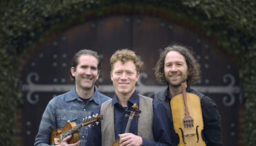 Folk/Classical group Lodestar Trio, holding stringed instruments, against a dark green backdrop