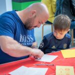 A man and boy do paper crafts on a red table