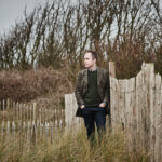 pianist Simon Callaghan stands against a background of fences and trees