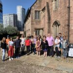 A tour group stands outside Chetham's Medieval buildings in the sunshine