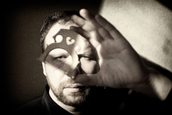 Sepia tone image of artist Petr Prause, holding a cello bridge in front of his face