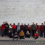 The singers of Kantos Chamber Choir, sitting/standing against a brick wall