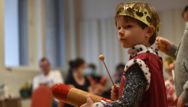 A small child in a medieval costume plays a small toy percussion instrument