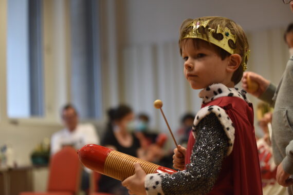 A small child in a medieval costume plays a small toy percussion instrument