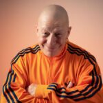 Comedian Jeff Innocent, wearing an orange top, against an orange background