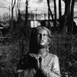 Lead image for show 'Hearing Voices' a black and white image of a statue of a women in prayer against a background of trees