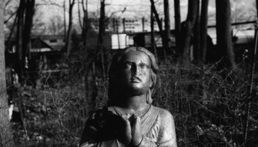 Lead image for show 'Hearing Voices' a black and white image of a statue of a women in prayer against a background of trees