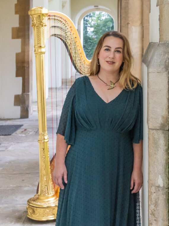 Musician Keziah Thomas stands in front of harp