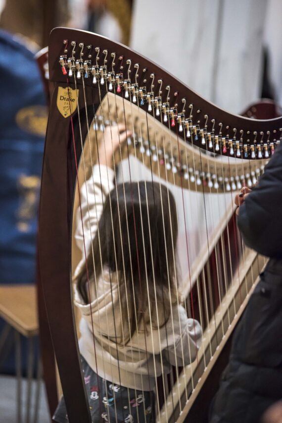 A small girl reaches for a lever on the top of a harp frame