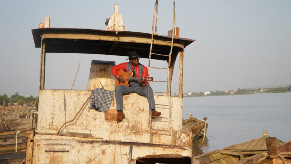 Artist Vieux Farka Toure on a boat with guitar