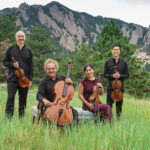 Takacs quartet standing in a field against a mountain backdrop, with instruments