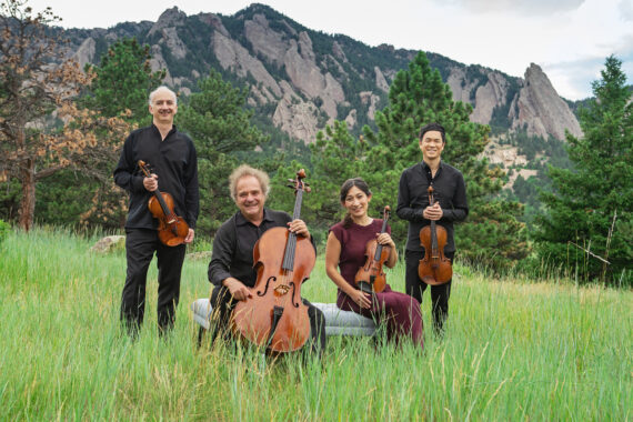 Takacs quartet standing in a field against a mountain backdrop, with instruments