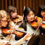 A group of girls playing violins in rehearsals.