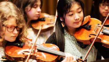 A group of girls playing violins in rehearsals.