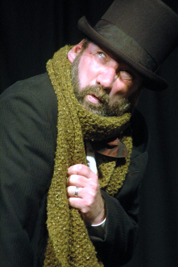 A bearded man in a thick green scarf and black top hat