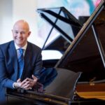 Charles Owen smiling next to a grand piano