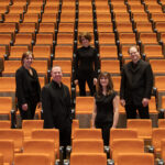 Musicians of the Pixels Ensemble, wearing black in an auditorium with orange chairs