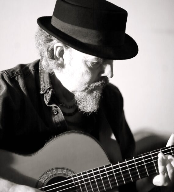 black and white image of Keith James, wearing a hat and playing guitar