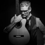 black and white photo of guitarist Jesse Cook with instrument