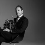 Black and white photo of musician Martin Owen with French Horn