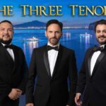 Three singers in dinner jackets against a seaside background