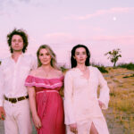 A man dressed in white, a woman dressed in pink and a woman dressed in white, standing on grass