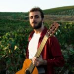 Artist Jesús Guerrero standing in a green field with a guitar