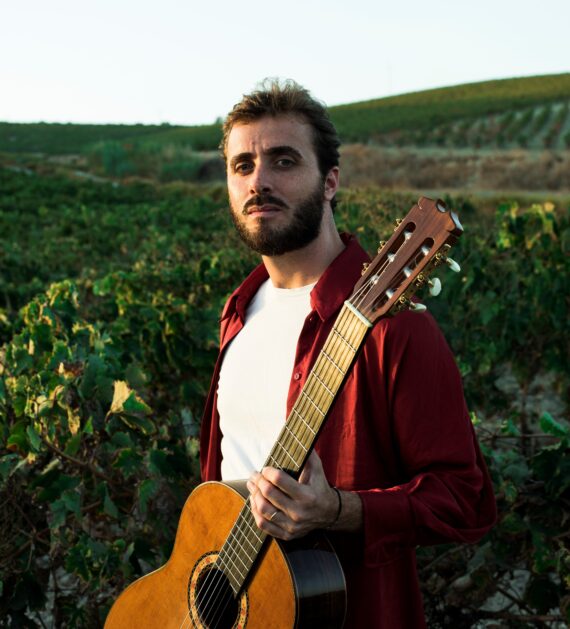 Artist Jesús Guerrero standing in a green field with a guitar