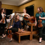 a group of musicians with string instruments sitting on a pile of wooden furniture