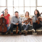 A group of four people seated holding string instruments