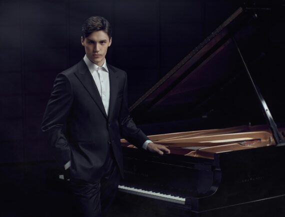 Jaeden Izik-Dzurko wearing a suit standing by a piano