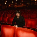 Pianist Brad Kella sitting on red seats in a theatre