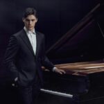 Jaeden Izik-Dzurko stands next to a piano