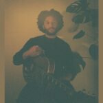 Musician Rory A Green, seated with guitar, on a sepia backdrop