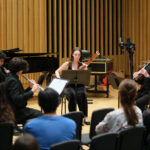 A group of students with instruments performing, with audience in front