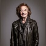 Headshot of singer Colin Blunstone, an older man with shoulder-length dark hair, smiling, wearing a leather jacket