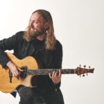 Mike Dawes (a man with long hair, dressed in black), playing guitar